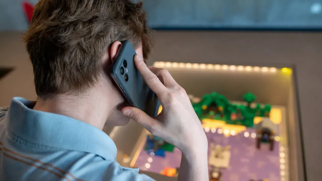 Person pratar i telefon, men det är inget ljud i telefonen vid samtal. Bakgrunden visar en upplyst display med en liten modellvärld.