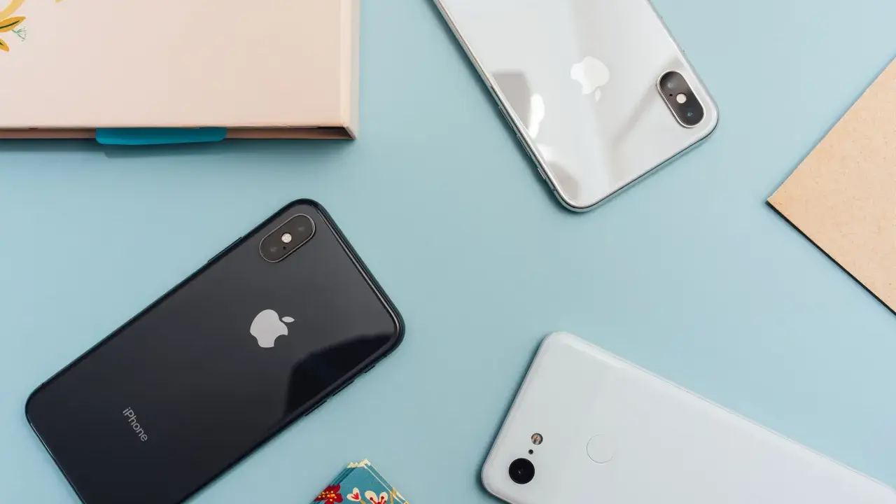 Två iPhones och en Android-telefon ligger på ett ljusblått underlag.