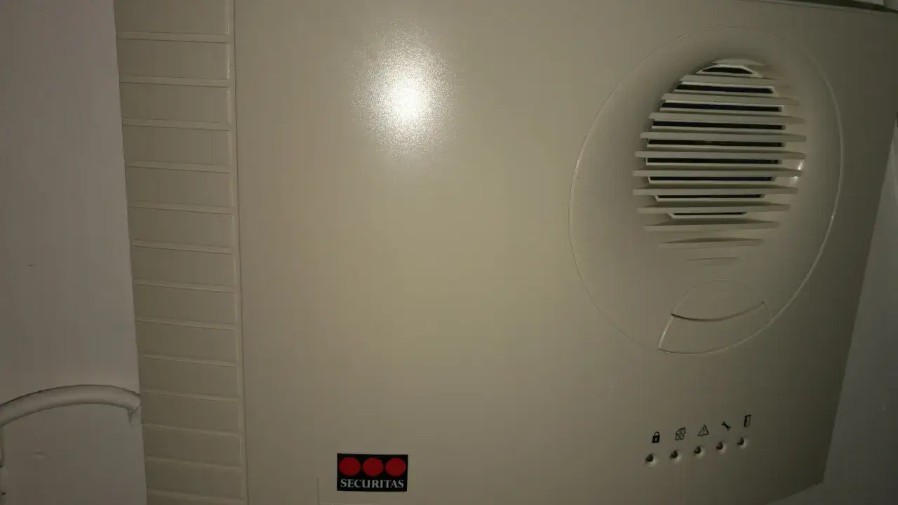 En vit Securitas huvudenhet, liknande en Verisure huvudenhet manual, med högtalargaller och statuslampor.