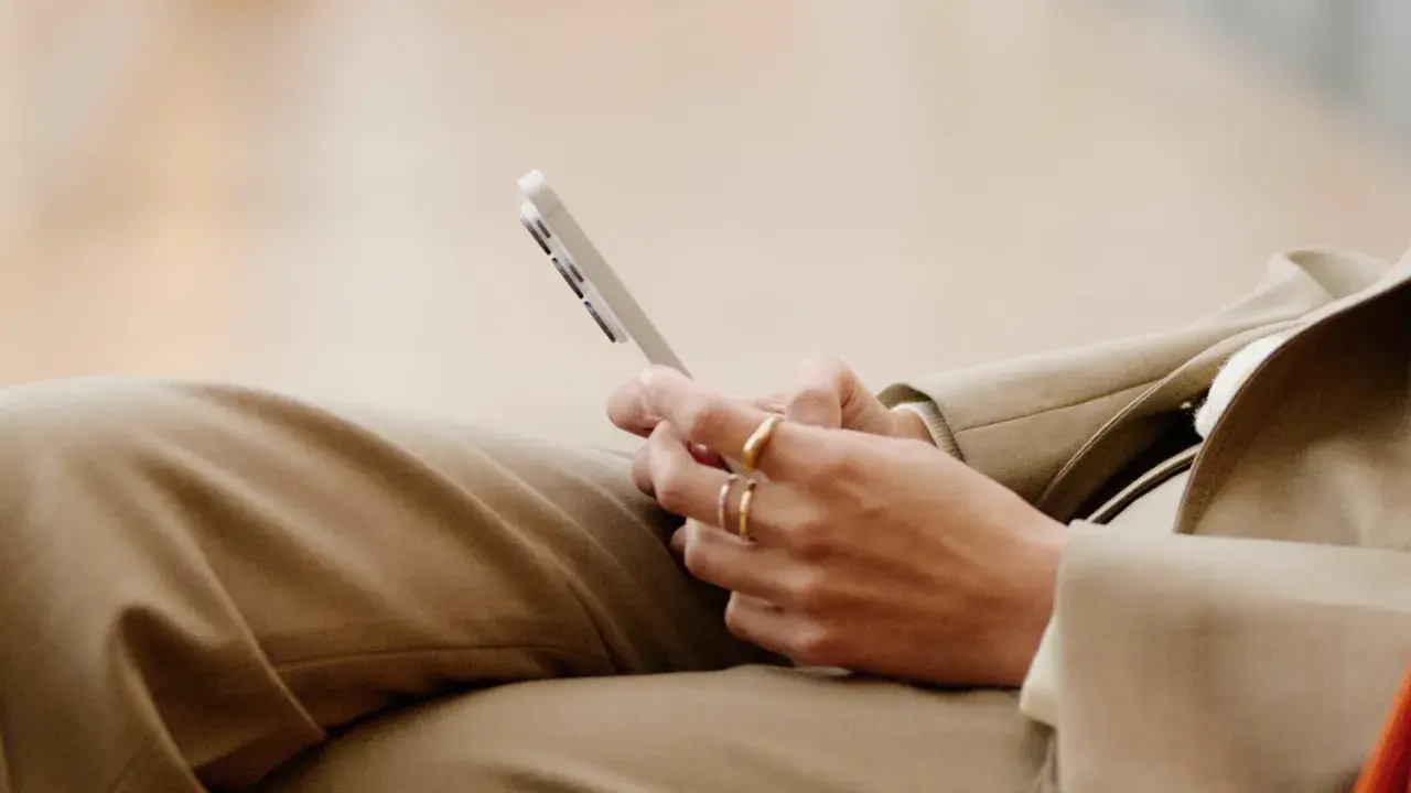 Person med ringar på fingrarna håller en mobiltelefon, kanske för att kolla sitt imei nummer.