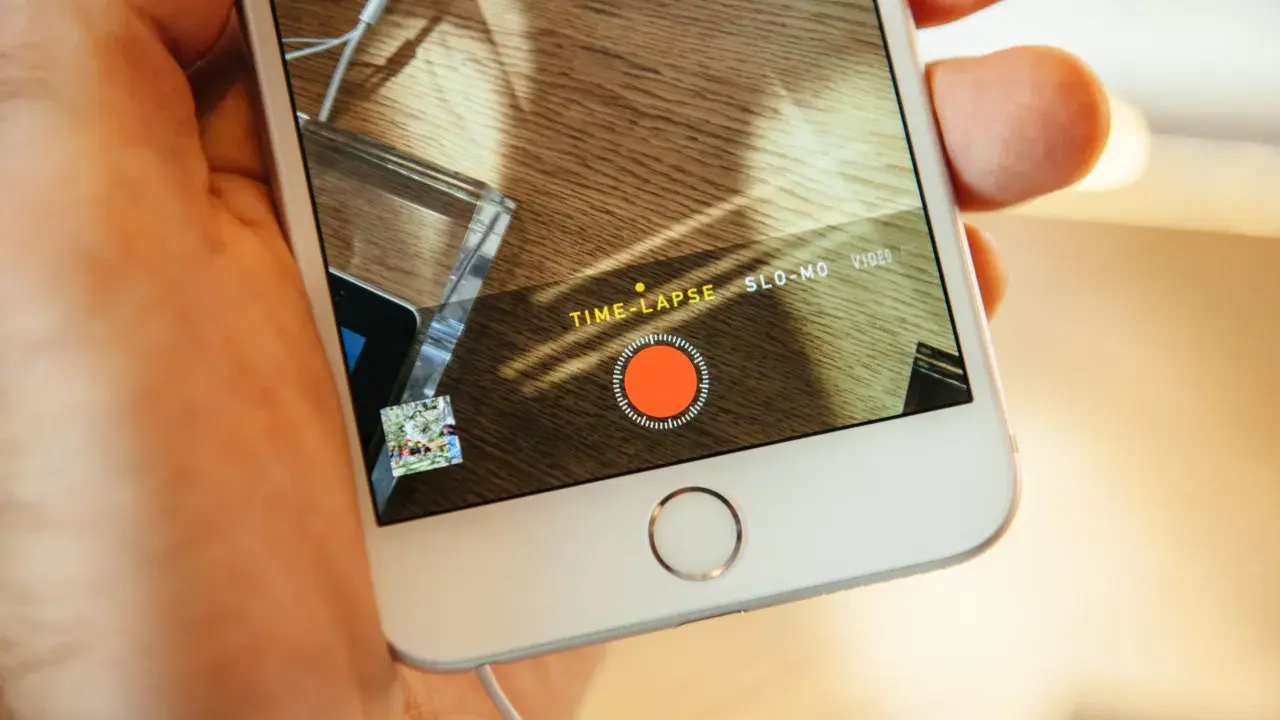En hand håller en iPhone med inspelningsläget TIME-LAPSE aktivt. En röd inspelningsknapp syns på skärmen.