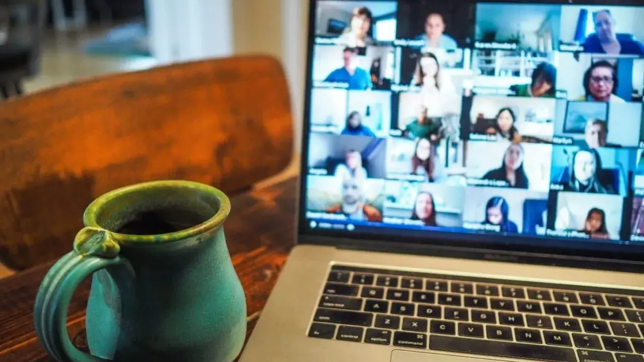 En kopp kaffe bredvid en laptop som visar ett videosamtal med många deltagare. Perfekt för distansarbete eller studier via android.