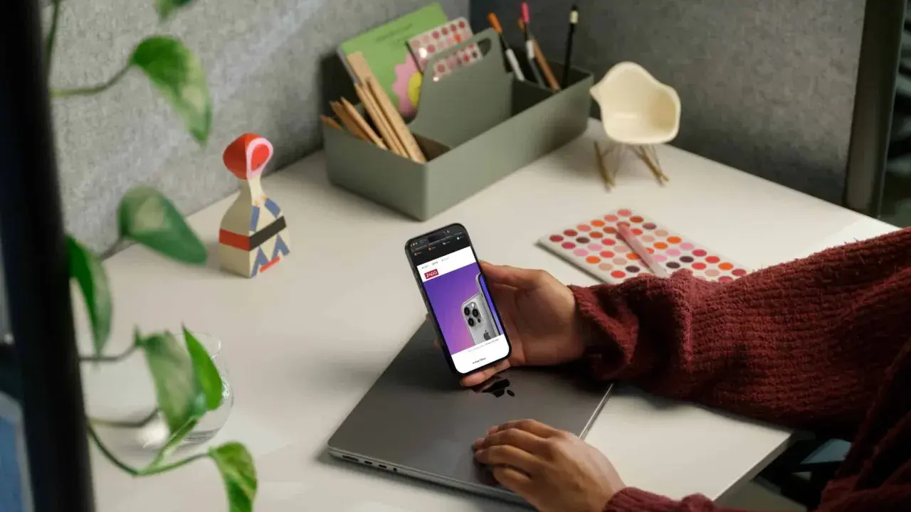 Person håller en iPhone med webbsida som visar en telefon, kanske för att jämföra aviseringar.