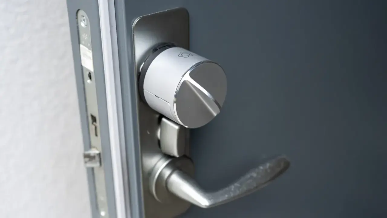 Detaljbild av en silverfärgad Verisure smart låsmodul installerad på en grå dörr.