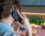 Person pratar i telefon, men det är inget ljud i telefonen vid samtal. Bakgrunden visar en upplyst display med en liten modellvärld.