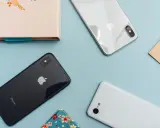Två iPhones och en Android-telefon ligger på ett ljusblått underlag.