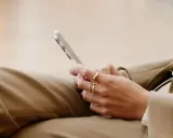 Person med ringar på fingrarna håller en mobiltelefon, kanske för att kolla sitt imei nummer.