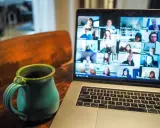 En kopp kaffe bredvid en laptop som visar ett videosamtal med många deltagare. Perfekt för distansarbete eller studier via android.