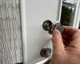 En hand håller en nyckel till en vit dörr, redo att aktivera den smarta låsmodulen.
