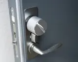 Detaljbild av en silverfärgad Verisure smart låsmodul installerad på en grå dörr.