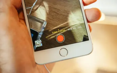 En hand håller en iPhone med inspelningsläget TIME-LAPSE aktivt. En röd inspelningsknapp syns på skärmen.