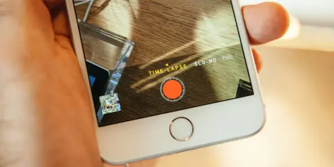 En hand håller en iPhone med inspelningsläget TIME-LAPSE aktivt. En röd inspelningsknapp syns på skärmen.