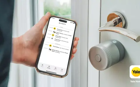 En hand håller en telefon med en Yale Doorman Bluetooth-app som visar aktivitetslogg. Dörren har ett modernt Yale-lås.