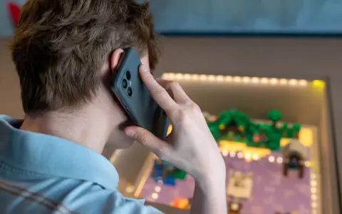 Person pratar i telefon, men det är inget ljud i telefonen vid samtal. Bakgrunden visar en upplyst display med en liten modellvärld.