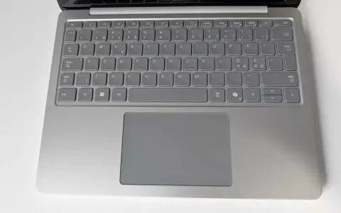 Grå laptop med tangentbord och styrplatta. Tangenterna har svenska tecken, inklusive å, ä, ö. Ett tankstreck syns på tangentbordet.