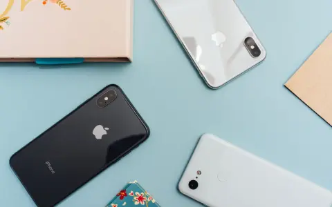 Två iPhones och en Android-telefon ligger på ett ljusblått underlag.