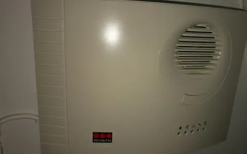 En vit Securitas huvudenhet, liknande en Verisure huvudenhet manual, med högtalargaller och statuslampor.