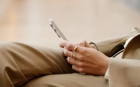 Person med ringar på fingrarna håller en mobiltelefon, kanske för att kolla sitt imei nummer.