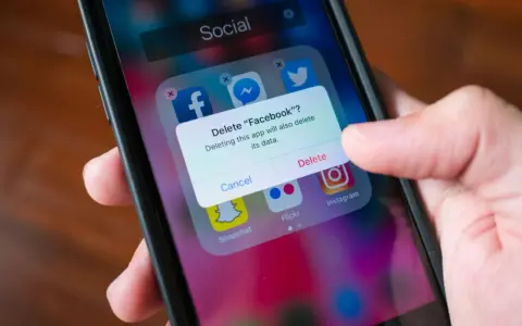 En finger trycker på "Delete" på en iPhone. En ruta frågar om man vill radera Facebook och dess data. Detta är inte hur man uppdaterar en app.