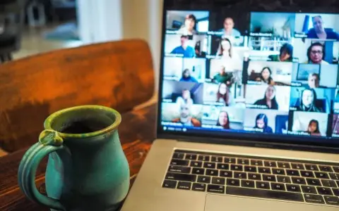 En kopp kaffe bredvid en laptop som visar ett videosamtal med många deltagare. Perfekt för distansarbete eller studier via android.