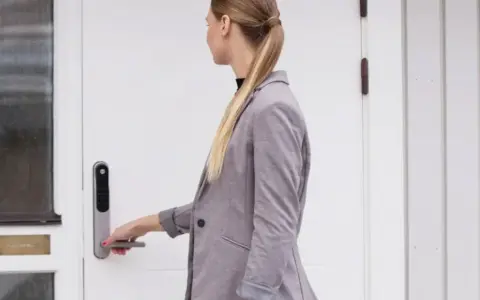 Kvinna med hästsvans öppnar en vit, gammal dörr med en Yale Doorman.