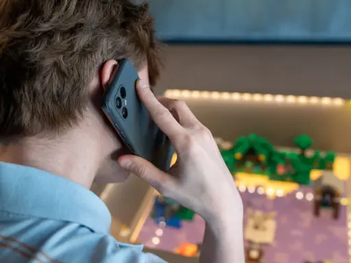 Person pratar i telefon, men det är inget ljud i telefonen vid samtal. Bakgrunden visar en upplyst display med en liten modellvärld.