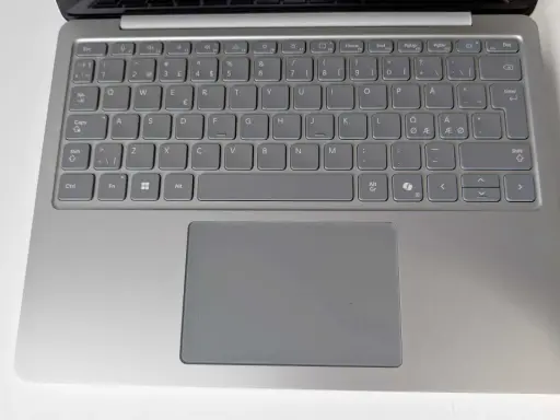 Grå laptop med tangentbord och styrplatta. Tangenterna har svenska tecken, inklusive å, ä, ö. Ett tankstreck syns på tangentbordet.
