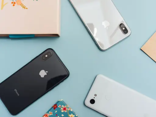 Två iPhones och en Android-telefon ligger på ett ljusblått underlag.