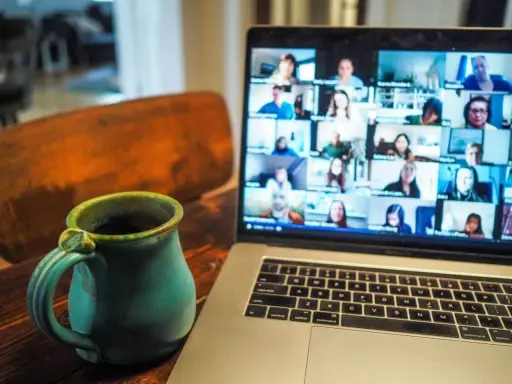 En kopp kaffe bredvid en laptop som visar ett videosamtal med många deltagare. Perfekt för distansarbete eller studier via android.