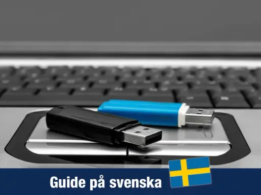 Två USB-minnen, ett svart och ett blått, ligger på ett tangentbord. En guide för Windows 11 USB på svenska.