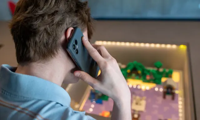 Person pratar i telefon, men det är inget ljud i telefonen vid samtal. Bakgrunden visar en upplyst display med en liten modellvärld.