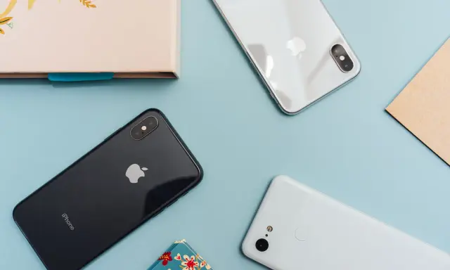Två iPhones och en Android-telefon ligger på ett ljusblått underlag.