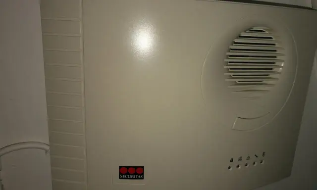 En vit Securitas huvudenhet, liknande en Verisure huvudenhet manual, med högtalargaller och statuslampor.