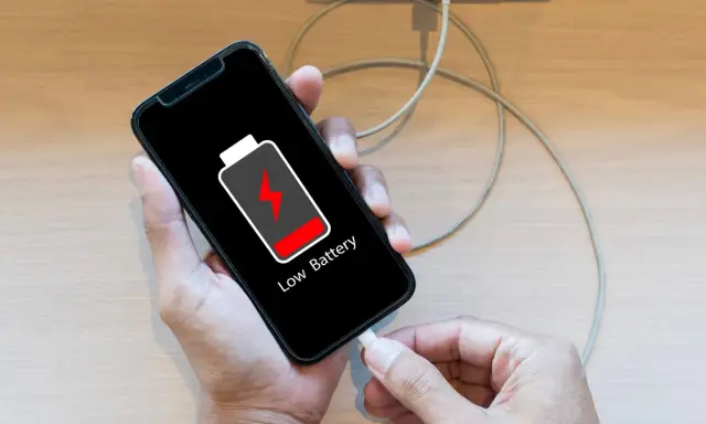 En person försöker ladda sin mobil, men den laddar inte. Batteriikonen visar låg nivå.