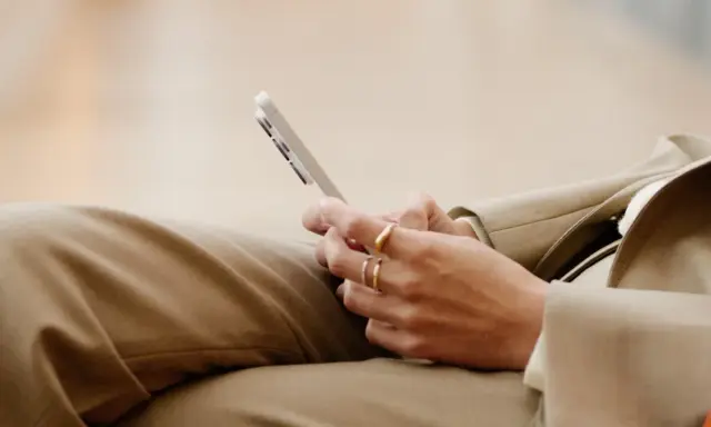 Person med ringar på fingrarna håller en mobiltelefon, kanske för att kolla sitt imei nummer.