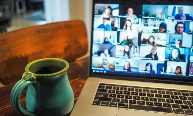 En kopp kaffe bredvid en laptop som visar ett videosamtal med många deltagare. Perfekt för distansarbete eller studier via android.