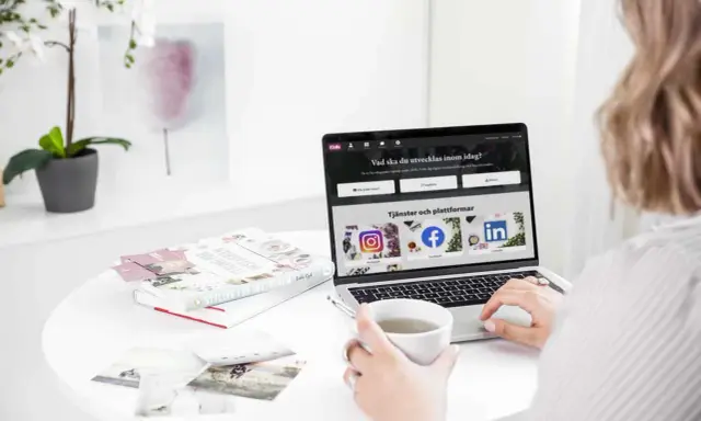 En person använder ett **publiceringsverktyg för sociala medier** på en laptop. På skärmen syns ikoner för Instagram, Facebook och LinkedIn.