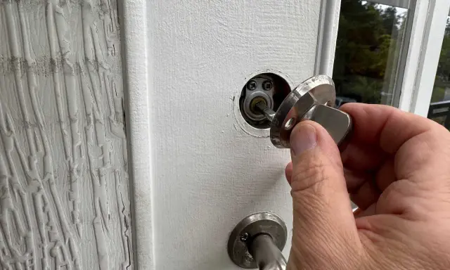 En hand håller en nyckel till en vit dörr, redo att aktivera den smarta låsmodulen.