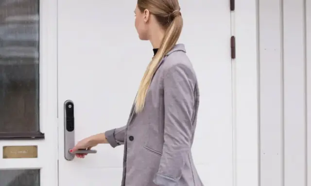 Kvinna med hästsvans öppnar en vit, gammal dörr med en Yale Doorman.