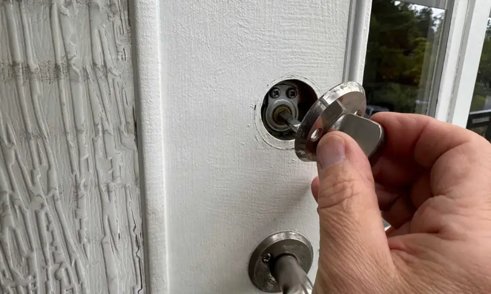 En hand håller en nyckel till en vit dörr, redo att aktivera den smarta låsmodulen.