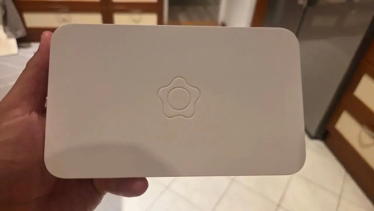 En hand håller en vit Verisure huvudenhet med wifi. En stiliserad blomma är präglad på ovansidan.