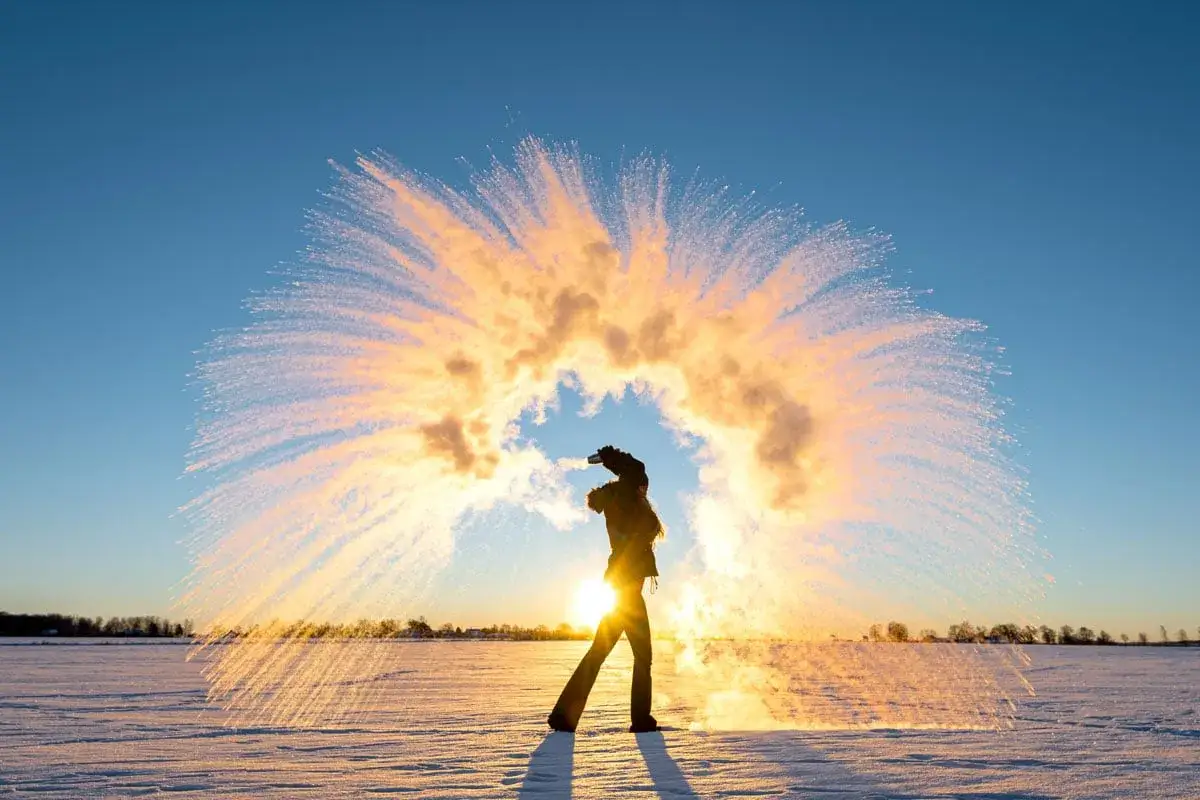 Person kastar varmt vatten i luften i kyla. Vattnet fryser till ispartiklar som lyser i solnedgången. En perfekt slutartid kamera fångar ögonblicket.