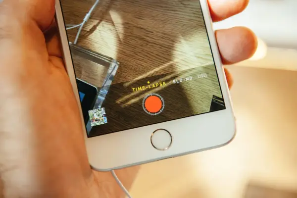 En hand håller en iPhone med inspelningsläget TIME-LAPSE aktivt. En röd inspelningsknapp syns på skärmen.